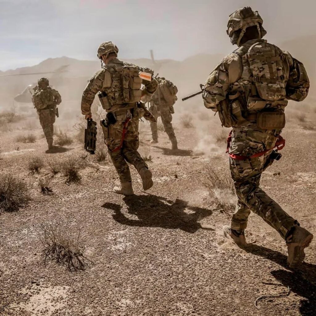 Modern soldiers wearing integrated soldier systems conducting a dismounted patrol in desert terrain.