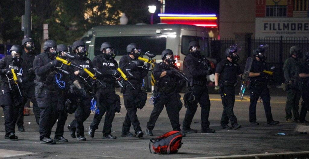 Public order police officers carrying PepperBall non-lethal launcher systems during tactical deployment