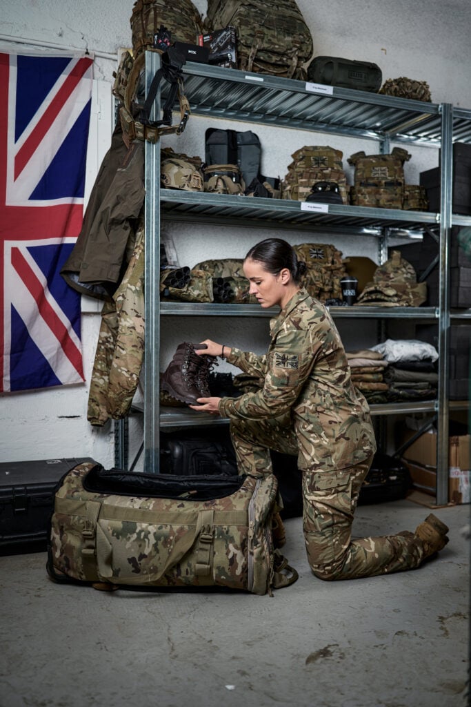 Female soldier in camouflage kneeling beside military equipment during an operational training exercise.